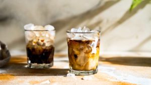 Iced Mokka Latte mit Eiswürfeln in einem Glas serviert. Im Hintergrund steht ein zweites Glas.