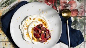 Labneh with caramelised beetroot, topped with walnuts and orange zest, served on a light plate.
